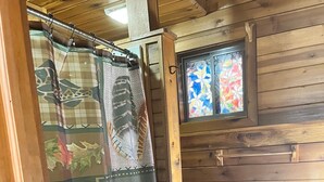 A bathroom with wooden walls, a shower curtain with animal prints, and a stained glass window. - NEW RIVER GORGE CABINS-ALMOST HEAVEN (Lansing)