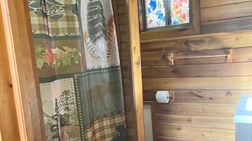 A bathroom with wooden walls, a shower curtain with animal prints, and a stained glass window.