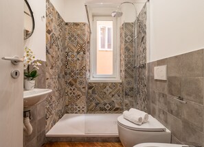 A bathroom with a shower, toilet, sink, and a window.