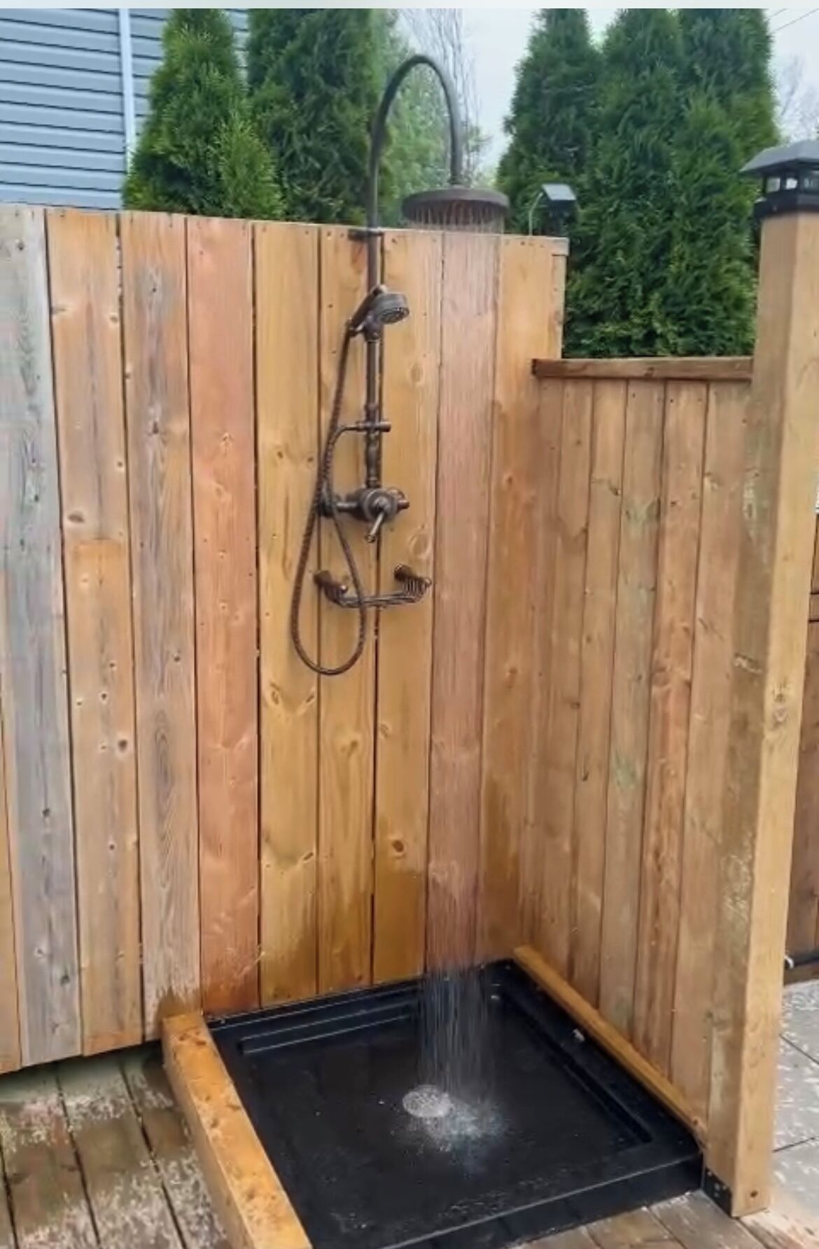 Un cerramiento de ducha exterior de madera con piso negro y un caño.