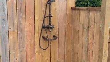 Un cerramiento de ducha exterior de madera con piso negro y un caño.