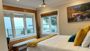 Un dormitorio con una cama grande, un banco y dos ventanas con vistas al mar.