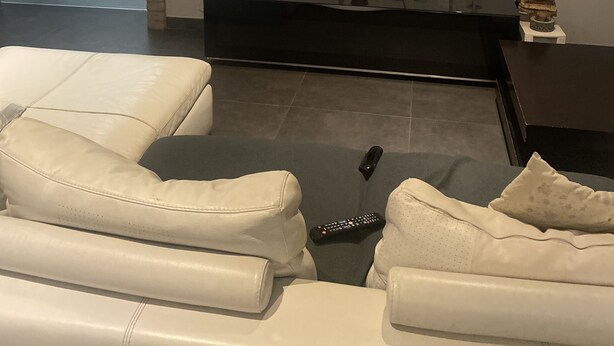 A modern living room with a large flat-screen TV mounted on the wall, a dark entertainment unit below, and a white leather sofa.