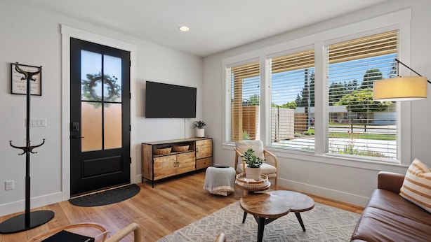 A modern living room with a wooden floor, a black door, a flat-screen TV, a sofa, a coffee table, and a window with blinds. - Holly Grove Cottage W/ Hot Tub (Vancouver)
