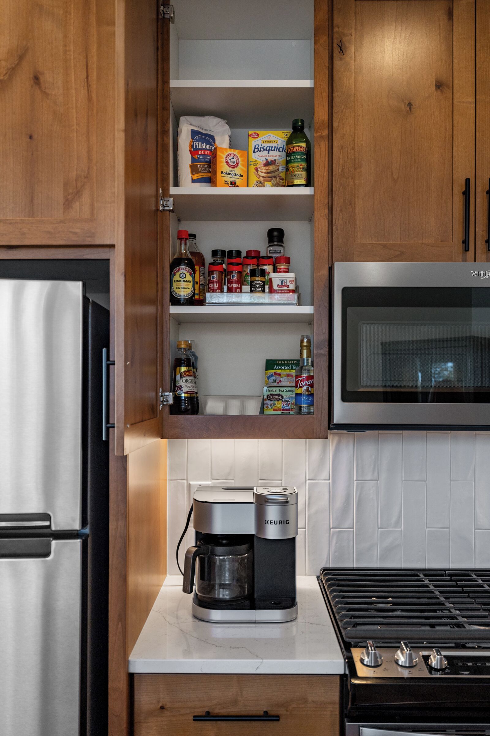 Una cocina con armarios de madera, microondas integrado, cafetera y varios utensilios de cocina en estantes.