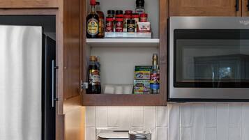 Una cocina con armarios de madera, microondas integrado, cafetera y varios utensilios de cocina en estantes.