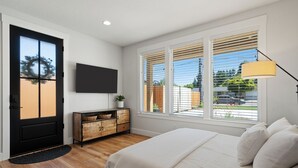 A bedroom with a bed, a TV mounted on the wall, a wooden cabinet, and a window with blinds. - Holly Grove Cottage W/ Hot Tub (Vancouver)