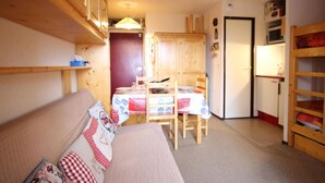A cozy room with a sofa, a dining table with chairs, wooden cabinets, and a small kitchenette. - 100m from ski slopes, Ground floor, balcony, ski locker, 24m², Chamrousse (Chamrousse)