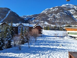 Schneebedeckte Landschaft mit Gebäuden, darunter eine Lodge mit Holzfassade und ein modernes Gebäude mit geneigtem Dach.