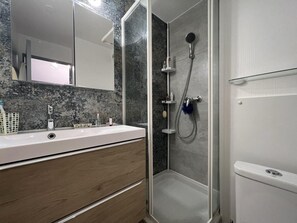Ein modernes Badezimmer mit Duschkabine aus Glas, einem weißen Waschbecken mit Marmorablage und Holzschränken.