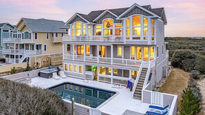 A multi-story beachfront house with a swimming pool, balconies, and a well-maintained lawn. - Oceanfront, Game Room, Decks, Heated Pool, Hot Tub, Ocean Views, Fully Loaded (Corolla)