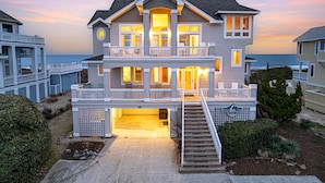 A two-story house with a balcony, a covered front porch, and a staircase leading to the entrance. - Oceanfront, Game Room, Decks, Heated Pool, Hot Tub, Ocean Views, Fully Loaded (Corolla)