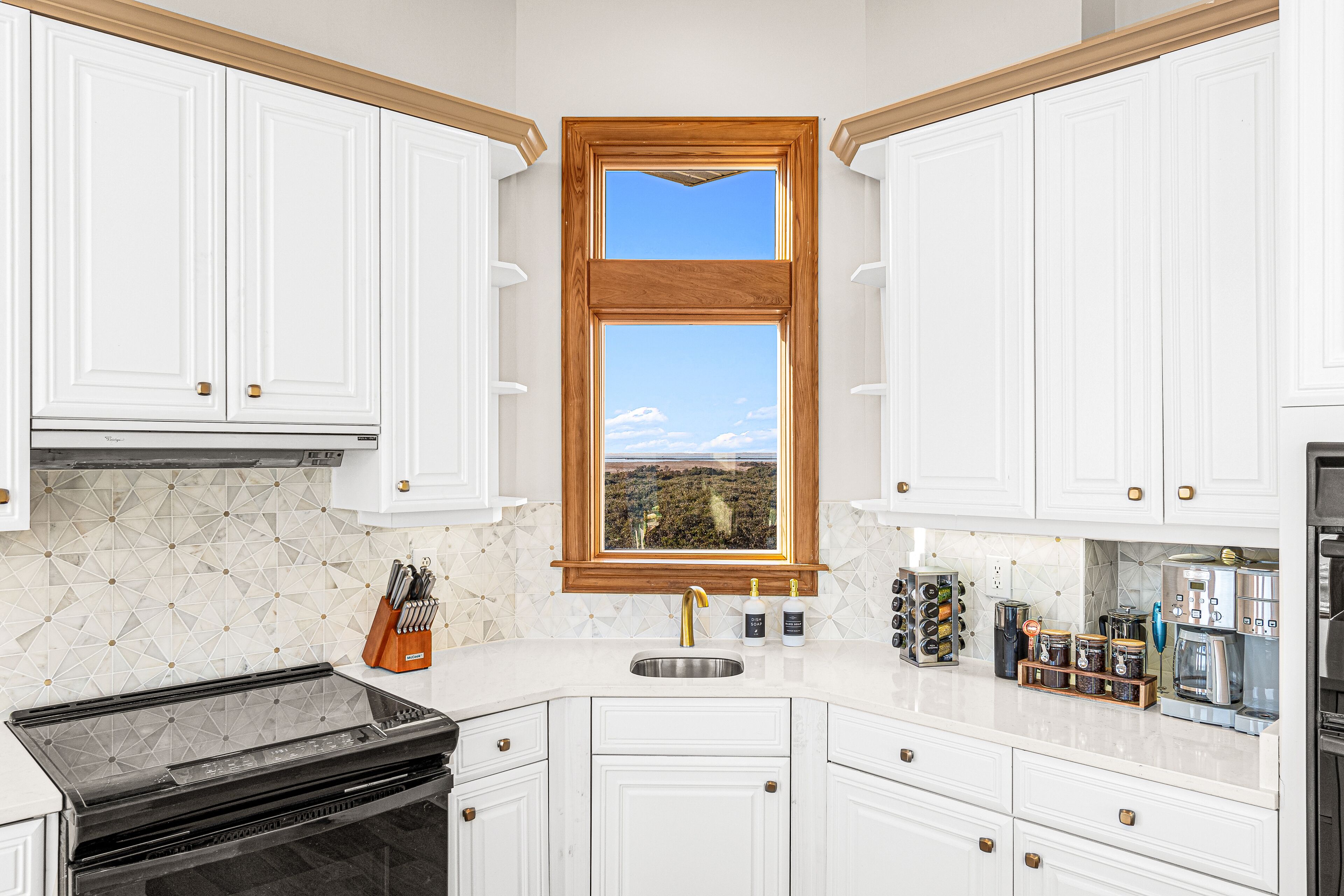 A kitchen with white cabinets, a double sink, a stove, and a window with a view of the outdoors.