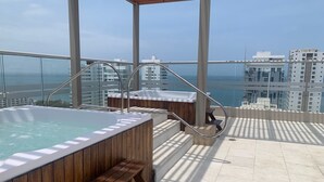 A rooftop terrace with a hot tub, wooden steps, and a view of the city and ocean. - Hermoso Apto en Santa Marta con Piscina (Gaira)