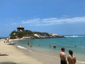 Ein Strand mit einer strohgedeckten Konstruktion auf einem Felsen.