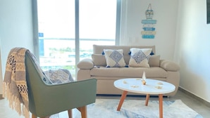 A living room with a sofa, a round coffee table, and a chair with a blanket. - Hermoso Apto en Santa Marta con Piscina (Gaira)