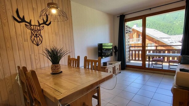 A wooden dining table with chairs, a TV, and a plant in a room with a wooden wall and a view of a wooden building outside. - Ski-in/ski-out & foot of the slopes, 6th floor, view mountain, swimming pool, sauna, balcony, tv (Les Orres)
