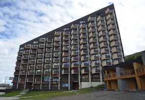 A multi-story building with balconies, a ground entrance, and a small adjacent structure with a wooden facade.