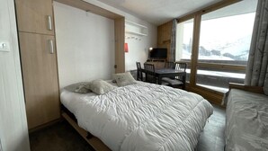 A compact bedroom with a bed, a desk, and a chair. There is a window with a view of a snowy landscape. - 10m from ski slopes, 6th floor, balcony, tv, ski locker, 19m², Les Menuires (Les Menuires)