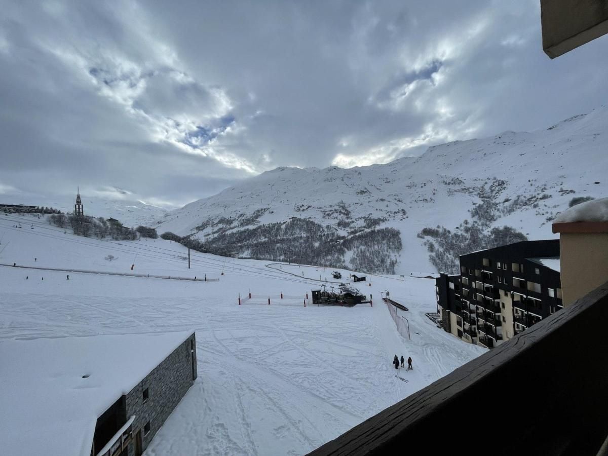 Pista d'esquí nevada amb un teleàs, edificis i un paisatge de muntanya de fons.