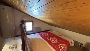 A small, cozy attic bedroom with a wooden ceiling, a single bed with a red and white bedspread, and a small window providing natural light. - 100m from ski slopes, 3rd floor, view open/ski slopes, tv, ski locker, 39m², Les Saisies (Les Saisies)