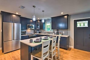 A modern kitchen with dark cabinets, stainless steel appliances, and pendant lighting.