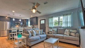 A modern living room with a grey sofa, a coffee table, and a dining area with a white table and chairs. - Pensacola Backyard Oasis 
January 2026 Pool Renovation (Gulf Breeze)