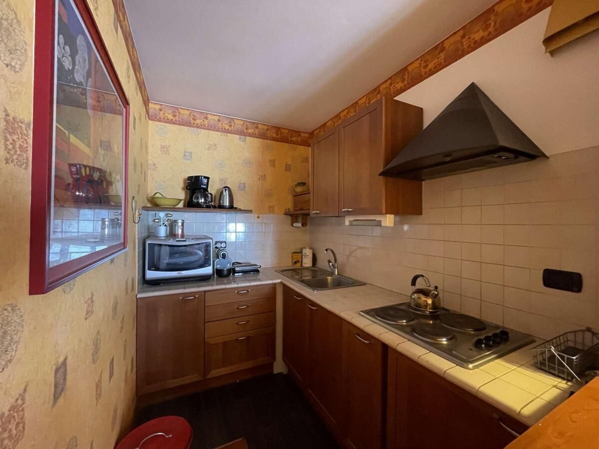 A compact kitchen with wooden cabinets, a microwave, a kettle, and a stove.