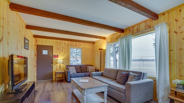 A cozy cabin interior with a wooden interior, a sofa, a coffee table, a TV, and a window with curtains. - Pet-Friendly Cabin Retreat: Wisconsin River Access (Mauston)