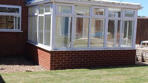 A conservatory with a brick base and multiple glass panes, attached to a brick wall. - 2 Bed House - Sleeps 4 - Pets - Garden - Parking (Newark)