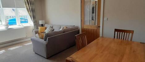Una sala de estar con un sofá, una mesa de comedor de madera y una ventana con cortinas.