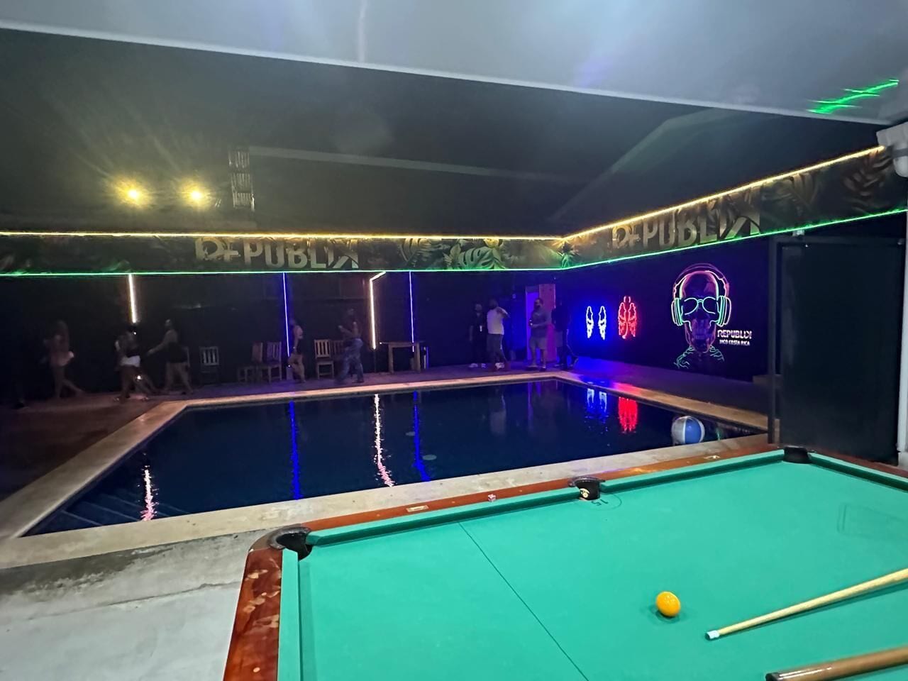 Una mesa de billar con un letrero de neón y una piscina en una habitación con poca luz.