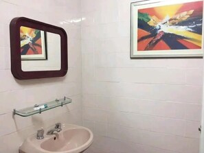 A bathroom with a sink, mirror, and two framed artworks on the wall.