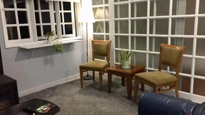 A living room with a blue sofa, two wooden chairs, a small table with a plant, and a window with white frames. - Cosy Selesa Hillhomes and Golf Resort (Bukit Tinggi)