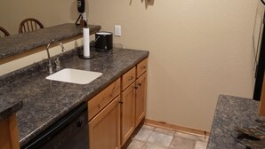 Une cuisine dotée de plans de travail en granit, d’un lave-vaisselle, de meubles en bois, d’une décoration murale en forme de feuille et d’une machine à café noire.