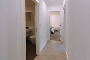 A narrow hallway with a toilet and a sink on the left, leading to a bedroom with a bed and a radiator.