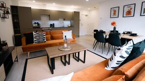 A modern living room with a sofa, coffee table, and dining area with chairs and a table set for two. - Two bedroom Central Apartment - ground floor (Exeter)
