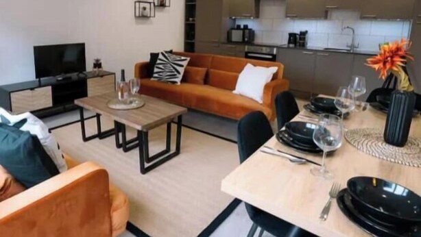 A modern living room with a sofa, coffee table, and dining area with a table set for two. - Two bedroom Central Apartment - ground floor (Exeter)