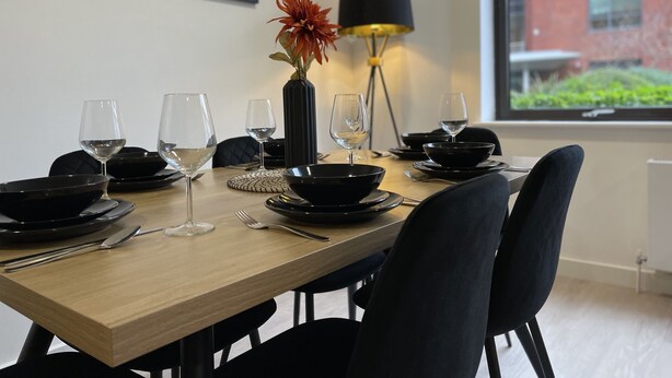 Une table à manger dressée avec de la vaisselle noire, des verres à vin et un vase contenant une fleur.