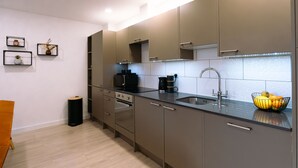 A modern kitchen with grey cabinets, a black countertop, a built-in oven, a sink, and a fruit bowl. - Two bedroom Central Apartment - ground floor (Exeter)