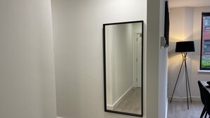 A modern room with a large mirror on the wall, a floor lamp, and a dining area with chairs. - Two bedroom Central Apartment - ground floor (Exeter)
