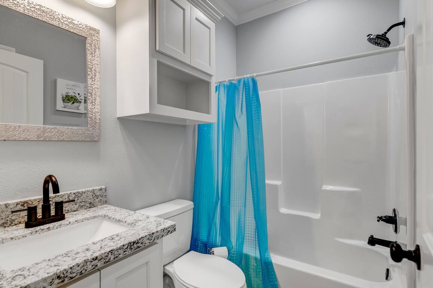 A bathroom with a white sink, a mirror, a toilet, and a shower with a blue shower curtain.
