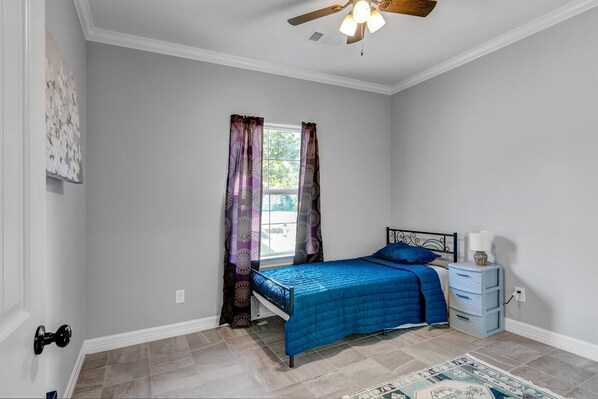 A bedroom with a bed, curtains, a ceiling fan, and a nightstand.