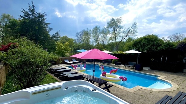 Un bain à remous doté d’un panneau de commande, une piscine avec des bouées en forme de licorne gonflable et des chaises longues.