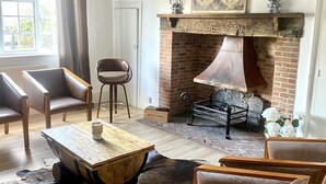 Une pièce rustique avec des poutres apparentes, une cheminée en briques, des fauteuils en cuir et une table en bois.