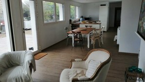A spacious living area with a dining table, two chairs, and a sofa. There is a kitchen area with a stove and cabinets in the background.