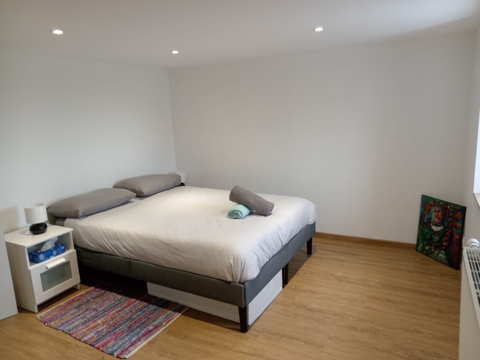 Un dormitorio moderno con cama, mesita de noche y una alfombra colorida.