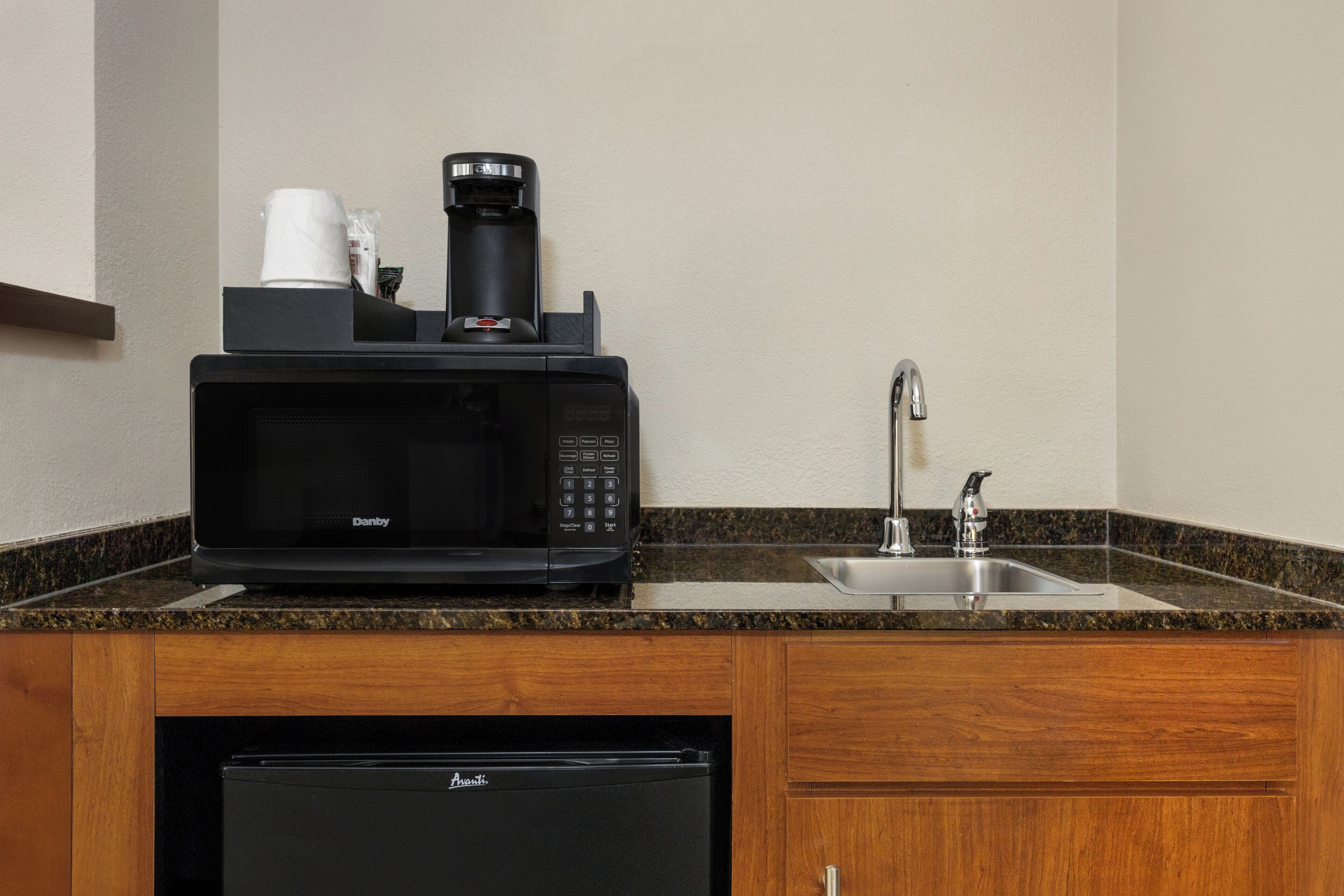Una cocina con microondas, cafetera y lavamanos.