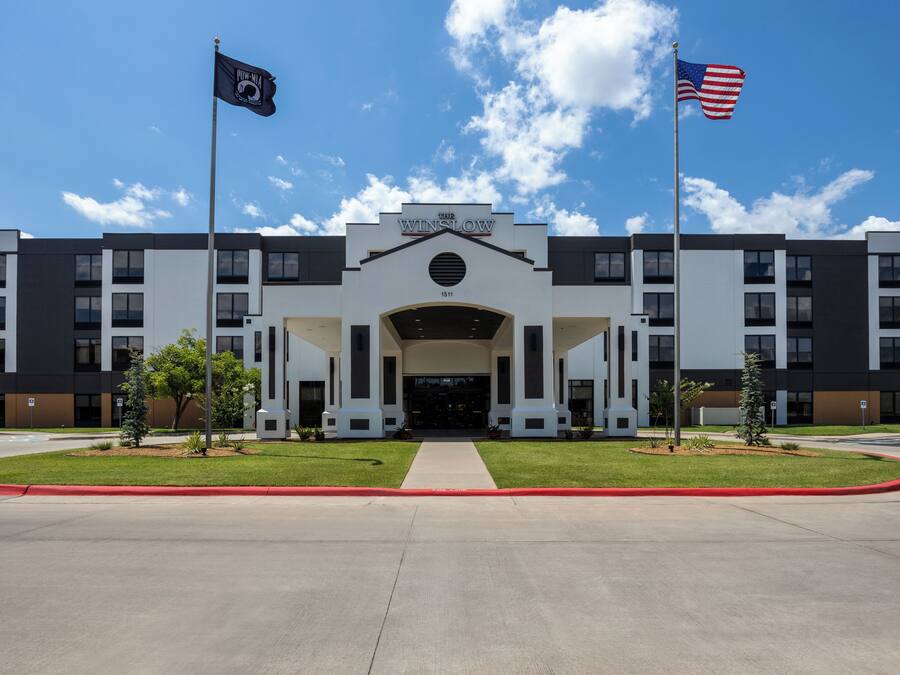 A modern building with a central entrance, two flags, and a well-maintained lawn.