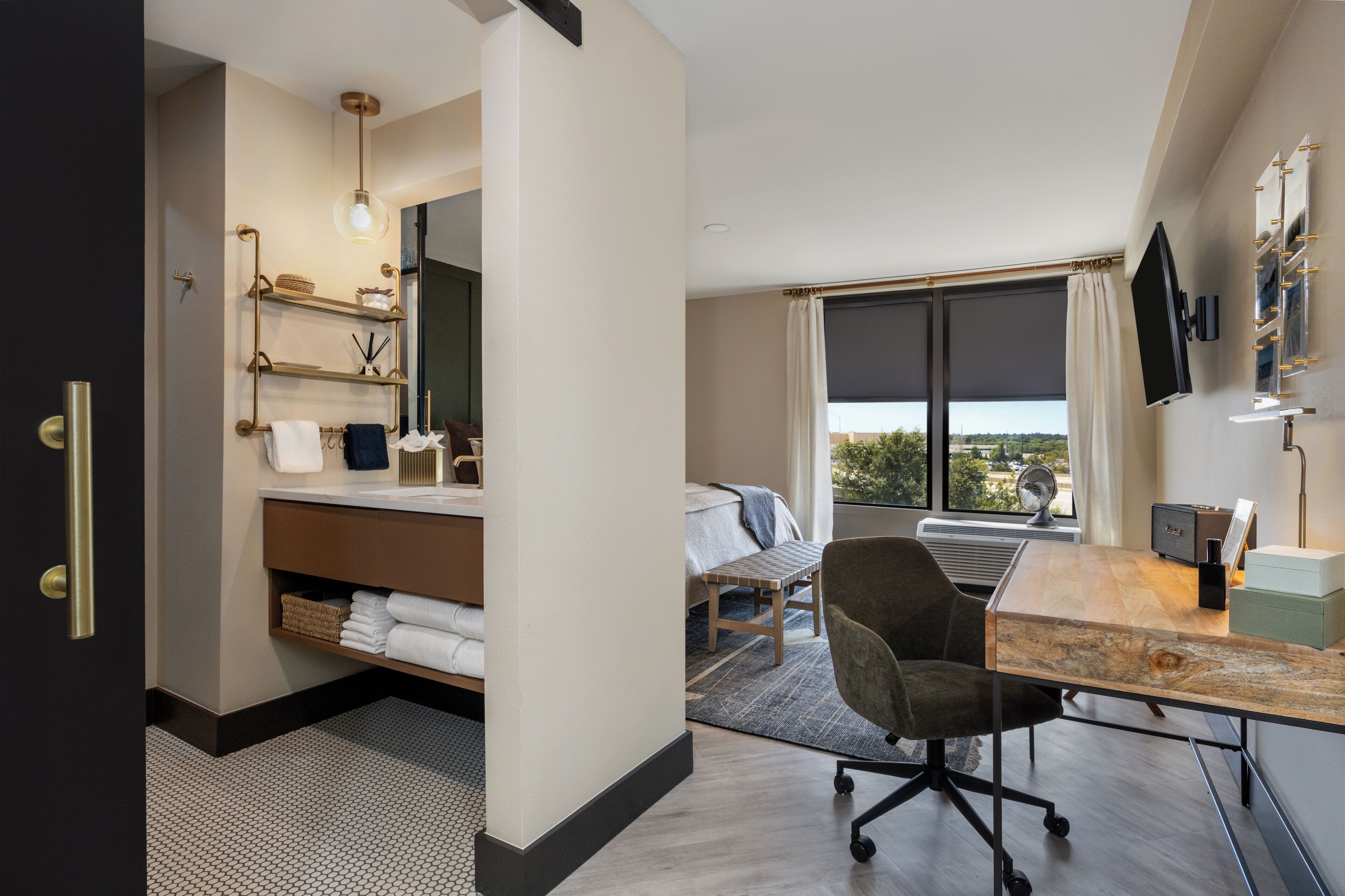 A modern hotel room with a bed, a desk, a chair, a TV, and a window with a view.